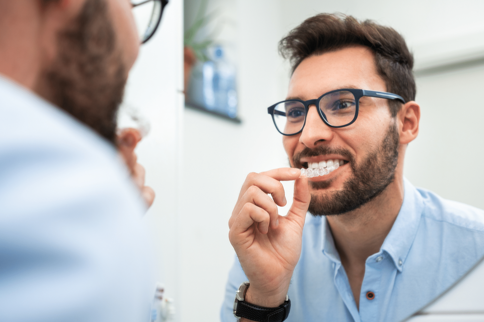 A smiling man looking in the mirror and holding a clear aligner