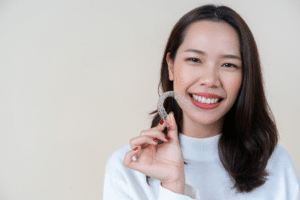 Smiling college-age woman holding a clear aligner near her face